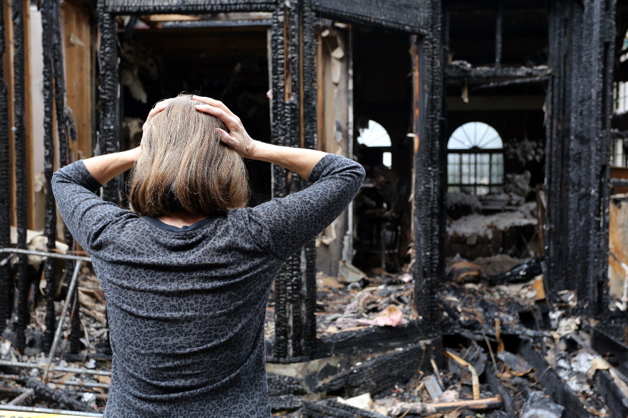 Picture of woman with hands on her head in front of a damaged building.